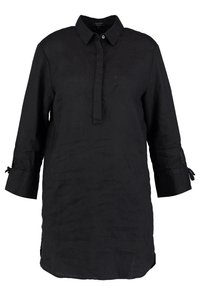 Zwarte linnen blouse met een kraag, driekwart mouwen en zijsplitten. Heeft een knopenlijst aan de voorkant en strikjes bij de mouwmanchetten.