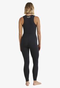 Traje de neopreno negro con un diseño sin mangas, textura suave y cremallera en la espalda. Presenta costuras en contraste y un logo en la parte superior de la espalda.