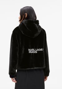 Black faux fur cropped hoodie with a front pocket. Features "KARL LAGERFELD JEANS" embroidered in white on the back. Soft texture.