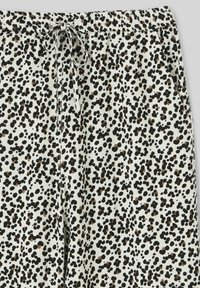 Pantalons en tissu blanc avec un motif specklé noir et marron. Dotés d'une taille élastique et d'un cordon de serrage ajustable pour le confort.