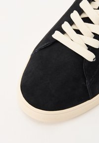 Sneaker in suede nero con punta arrotondata, lacci color crema e suola in gomma testurizzata. Finitura liscia con dettagli di cucitura minimi.