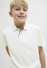 Polo shirt blanc avec un col texturé, présentant un accent marine et un petit logo cousu sur la poitrine. Manches courtes et tissu doux.