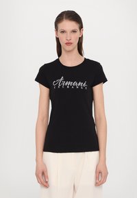 Schwarzes Baumwoll-T-Shirt mit kurzen Ärmeln, auf der Vorderseite mit einem silbernen Glitzer-Logo "Armani Exchange". Glatte Textur, klassischer Schnitt.