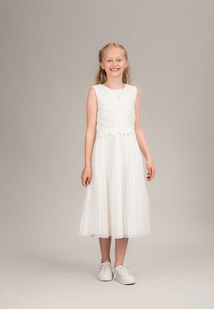 Weißes Kleid mit einem Spitzenoberteil und plissiertem Rock, kombiniert mit weißen Turnschuhen. Einfaches Design und bequeme Materialien.