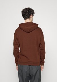 Brown hoodie with a kangaroo pocket, adjustable hood, ribbed cuffs, and a relaxed fit. Made from soft, textured fabric.