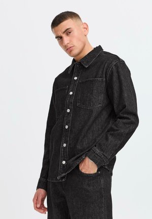 Black denim jacket featuring a collared neckline, front buttons, and two chest pockets with slightly frayed edges. Smooth texture.