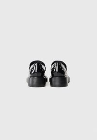 Chaussures en cuir verni noir avec une finition lisse, dotées d'œillets décoratifs et d'une semelle noire épaisse et texturée. Logo embossé sur le talon.