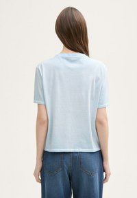 Tricou din bumbac de culoare albastru deschis, cu mâneci scurte, guler la bază și o croială lejeră. Culoare puțin scurtată. Simplu, fără modele sau ornamente.