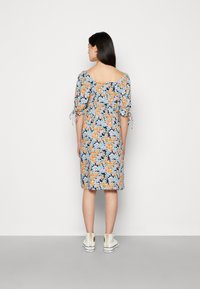 Vestido com estampado floral, mangas curtas bufantes, cintura ajustada e costas quadradas. As cores predominantes são azul, laranja e verde. Usado com ténis brancos.