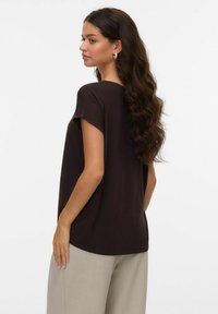 Chemise marron à manches courtes avec une coupe décontractée et un col rond. Le tissu semble doux avec des coutures minimales, portée avec un pantalon clair.