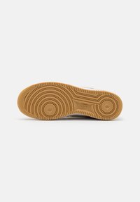 Sneaker outsole with a gum rubber sole featuring circular tread patterns and raised textures; light color scheme with branding.