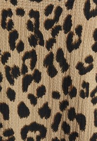 Textilie s leopardím vzorem, která se vyznačuje texturovaným béžovým pozadím s hustě uspořádanými černými a hnědými skvrnami, zdůrazňující hmatový design.