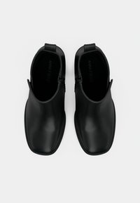 Bottines noires à la cheville au design épuré, fabriquées en matériau lisse, dotées d'une fermeture éclair latérale et d'une forme arrondie à l'avant. Aucun motif visible.