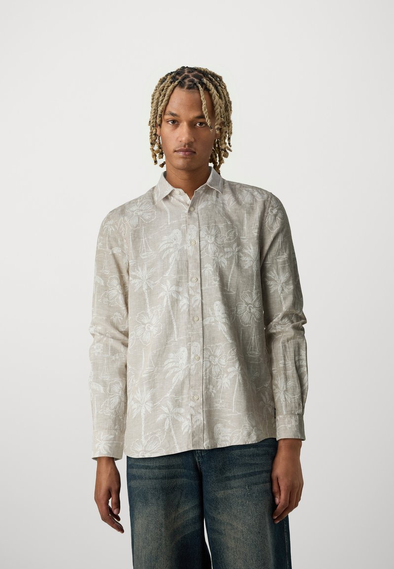 Lichtbeige langemouwen shirt met een subtiel tropisch bloemenpatroon, met knoopsluiting aan de voorkant en een ontspannen pasvorm, gestyled met blauwe spijkerbroek.
