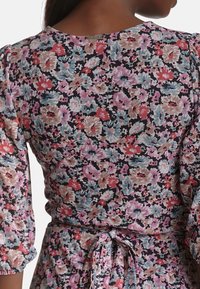 Látka s květinovým vzorem v odstínech růžové, modré a černé. Má vypolstrované rukávy a pásek v pase, s výstřihem do kulata na zádech.