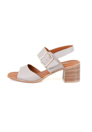 Sandal en cuir gris avec un bout ouvert, accent de grande boucle, et une semelle intérieure en cuir beige. Le talon carré est texturé avec des rayures horizontales.