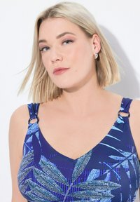 Haut de maillot de bain à motifs bleus avec un design en v, des bretelles ajustables avec un matériel circulaire et un motif de feuilles texturé.