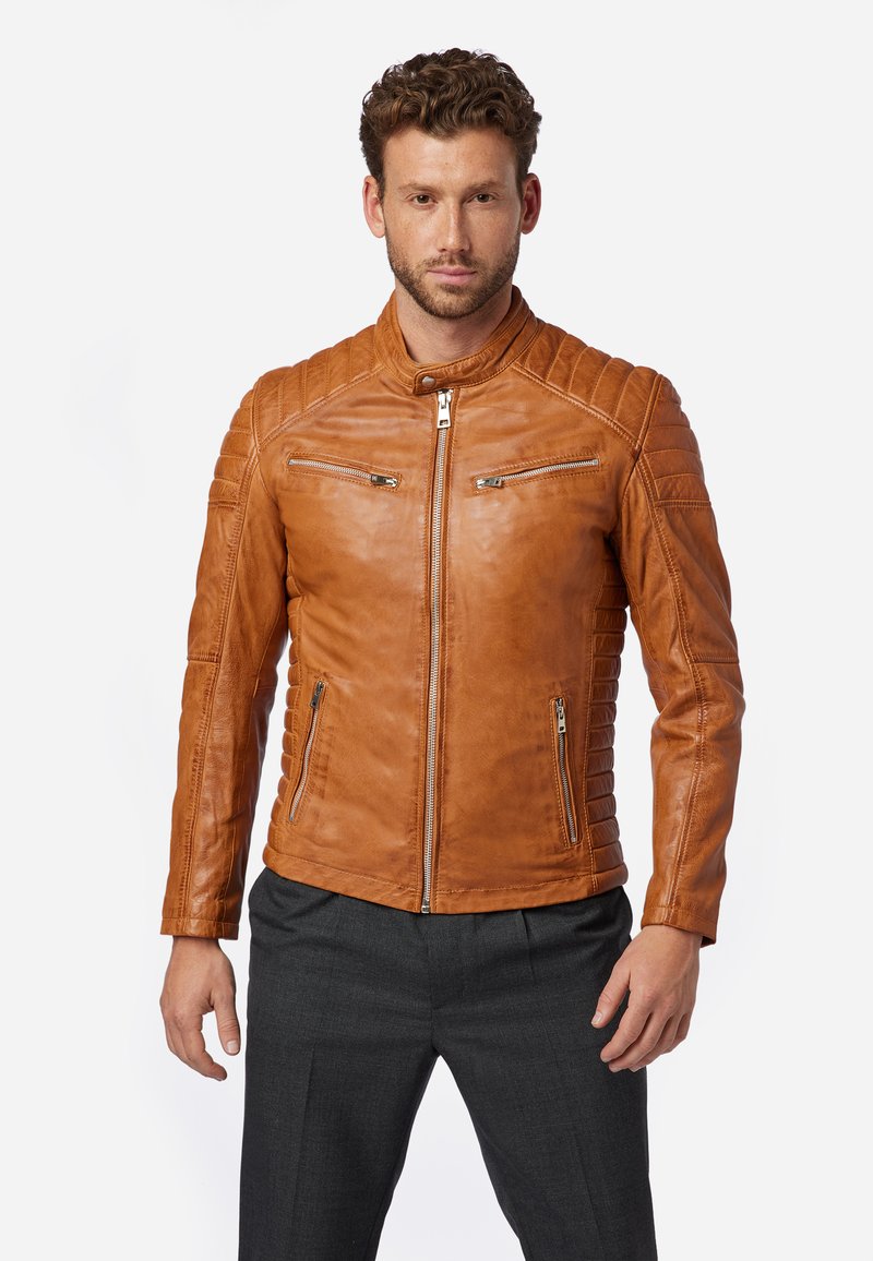 Tan leren jack met gequiltte schouders en ritszakken. Heeft een staande kraag en een gladde textuur. Voorzien van een ritssluiting aan de voorkant.