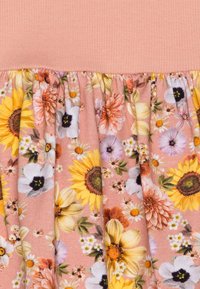 Květnové šaty s broskvovým žebrovaným korzetem a nařasenou květinovou sukní, která obsahuje slunečnice, sedmikrásky a pastelové květiny na růžovém pozadí.