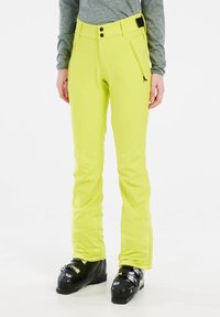 Neon gele skibroek met een slim fit, twee met rits afgesloten zakken, een verstelbare tailleband en op maat gemaakte pijpen voor een slank ontwerp. Zwarte skibotten worden gedragen.