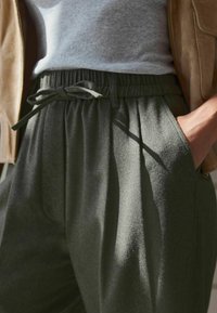 Pantalons plissés vert foncé avec une finition texturée. Dotés d'une taille élastique avec cordon de serrage à nouer et de poches latérales.