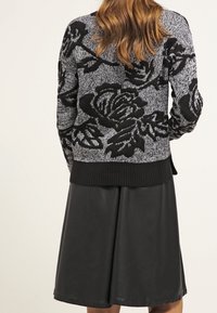 Czarny i biały sweter w wzory z kwiatowym wzorem, pleciona tekstura, ściągacz u dołu, zestawiony z gładką, czarną spódnicą do kolan.