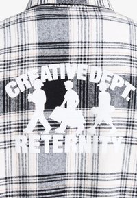 Chemise à carreaux blanche, noire et orange, avec un motif blanc représentant trois silhouettes et le texte "CREATIVE DEPT. RETERNITY."