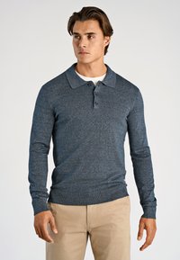 Granatowy longsleeve polo z teksturowanym splotem, trzema guzikami oraz prążkowanymi mankietami, zestawiony z beżowymi spodniami.