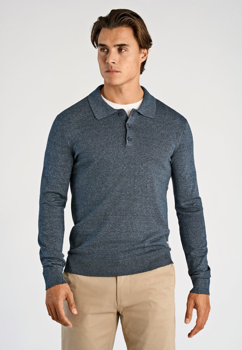 Granatowy longsleeve polo z teksturowanym splotem, trzema guzikami oraz prążkowanymi mankietami, zestawiony z beżowymi spodniami.