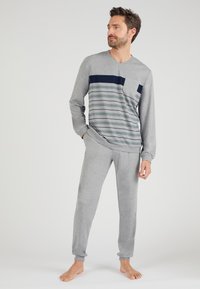 Camiseta de manga larga gris con diseño a rayas en azul oscuro y verde, combinada con pantalones jogger grises. Tejido suave, corte relajado, puños elásticos.