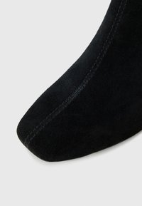 Black suede ankle boot featuring a pointed toe and subtle stitching detail. The surface has a soft, textured appearance.