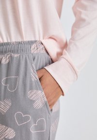 Ljusrosa långärmad tröja i kombination med grå joggers med ljusrosa hjärtan. Mjuk tygkvalitet, elastisk midja och sidoficka.