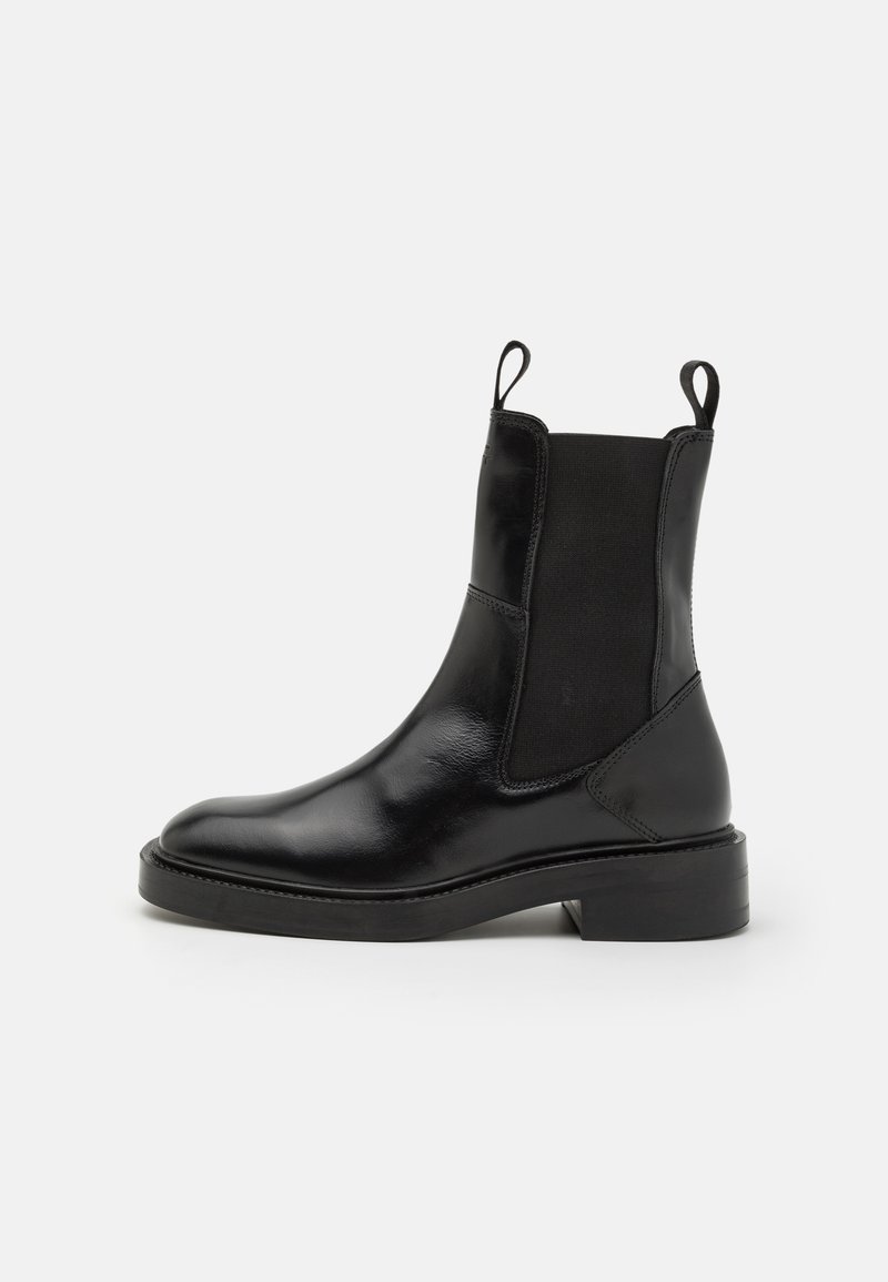 Black leather ankle boot with elastic side panels, round toe, and pull tabs; flat sole with a moderate heel. Smooth texture and sleek design.