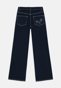 Bredde ben mørke denim jeans med hvite sømmer. Har to baklommer, hvorav den ene er prydet med blomsterbroderi.