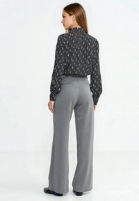 Czarna bluzka z długim rękawem w pionowe wzory, w połączeniu z szarymi spodniami o szerokich nogawkach. Gładka tkanina, dopasowany krój, spodnie długości do kostek.