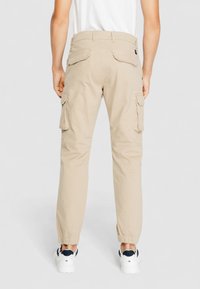 Beige Cargo-Hosen mit schmalem Schnitt, elastischen Bündchen und Seitentaschen. Hergestellt aus leichtem Stoff, entworfen für Funktionalität und Komfort.