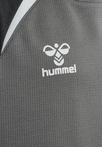 Gros plan sur un tissu de sport gris avec le logo de la marque hummel en blanc et un emblème d'abeille stylisée.