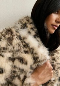 Nepbonten jas met een beige achtergrond en bruine luipaardvlekken, met een zachte, pluizige textuur en een grote kraag voor extra warmte.