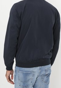 Chaqueta bomber de nylon azul marino con puños y cintura acanalados. Diseño simple sin logotipos ni patrones visibles. Textura ligera y suave.