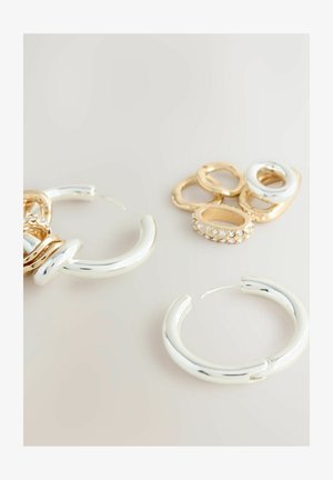 Silberne Creolen mit einer glatten, reflektierenden Oberfläche neben goldenen und silbernen Ringen, darunter einer mit klaren Strasssteinen.