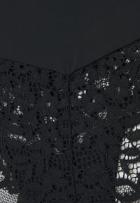 Black garment featuring a smooth top section and intricate black lace detailing at the bottom, showcasing floral patterns and a textured finish.