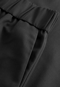 Mustan kankaan sileä pinta, jossa on kerrottu vyötärö ja hienovarainen kiilto. Materiaali näyttää kevyeltä ja joustavalta.