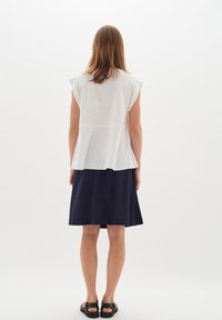 Fehér peplum felső, rövid ujjú, sötét tengerészkék szoknyával párosítva, amely térd hosszúságú és lazább fazonú. Texturált anyag.