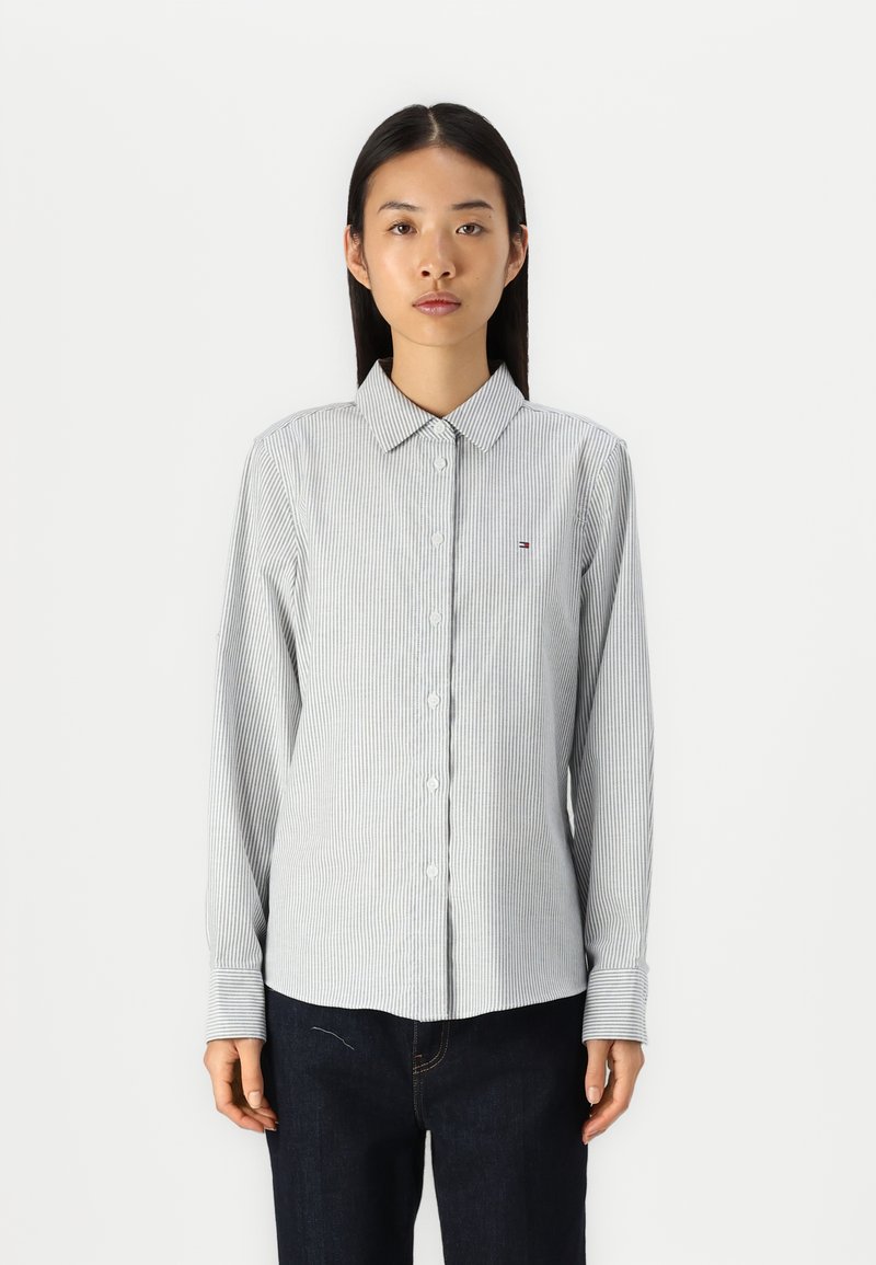 Camicia con bottoni caratterizzata da strisce verticali blu e bianche, colletto classico, maniche lunghe e un piccolo logo ricamato sul petto.