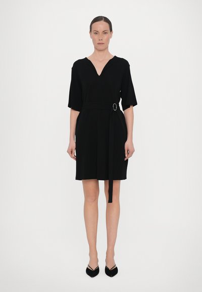 Schwarzes Kleid mit V-Ausschnitt, kurzen Ärmeln, tailliert mit einem Gürtel und Ringdetail. Glatte, einfarbige Struktur. Knielanges Design.