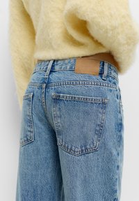 Világoskék farmernadrág magas derékkal, két hátsó zsebe van, és a derékvonalán egy bőr címke található, melyen az márkaneve domborítva szerepel.