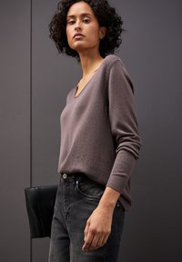 Sweter w stonowanym mauve, dekolt w kształcie litery V, długie rękawy, ściągacze na mankietach. W połączeniu z czarnymi dżinsami z wysokim stanem i czarną kopertówką.