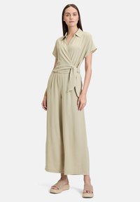 Lys beige wrap jumpsuit med korte ærmer, sn�øring i taljen og bred ben-designet, parret med beige platform sandaler. Glat tekstur.