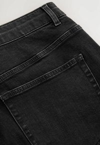 Gros plan sur un jean en denim noir montrant la poche arrière, la boucle de ceinture et les coutures détaillées sur la texture du tissu.