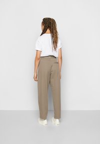 Lichtgrijs t-shirt, relaxte pasvorm, gecombineerd met hoge beige broeken met een achterzak, afgewerkt met witte sneakers.